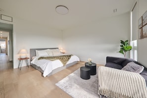 A modern bedroom with a large bed, bedside tables, a sofa, and a potted plant.