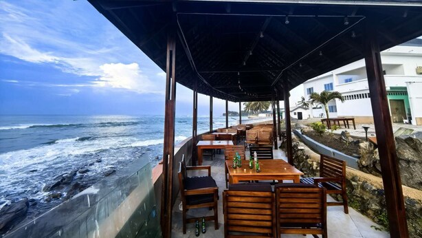 An outdoor seating area with wooden tables and chairs, overlooking the ocean. - Joy Beach Lodge (Sekondi-Takoradi)