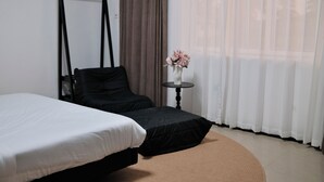A bedroom with a bed, a chair, a small table with a vase, and a window with curtains. - Joy Beach Lodge (Sekondi-Takoradi)