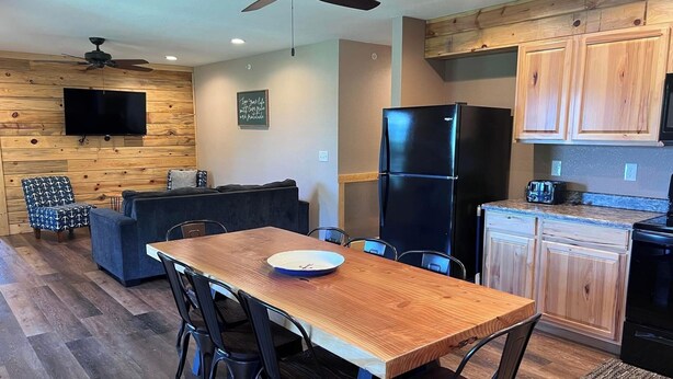 Une cuisine moderne avec des meubles en bois, un réfrigérateur noir et un coin repas comprenant une table et des chaises en bois.