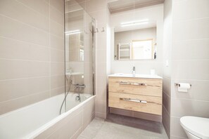 Une salle de bain moderne avec une douche à parois de verre, un meuble-lavabo en bois doté de tiroirs et des toilettes blanches.