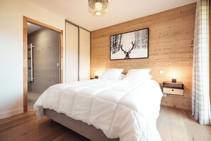 Une chambre à coucher avec un lit, des murs en bois, un tableau encadré, des lampes de chevet et une porte donnant sur une salle de bain.