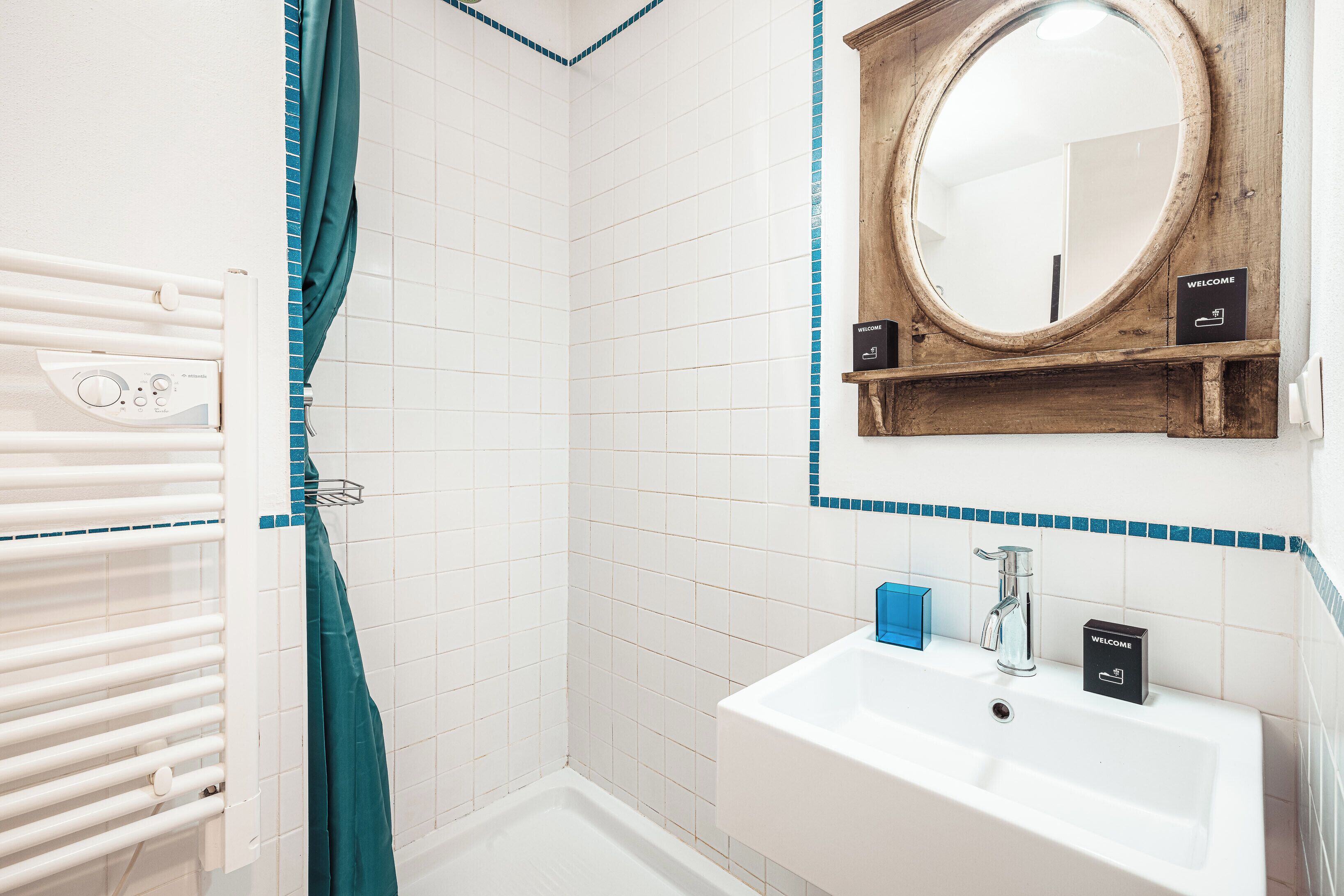 A bathroom with a white sink, a wooden-framed mirror, and a shower with a teal curtain.