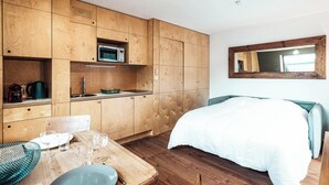 A compact room with wooden cabinetry, a bed, a dining table with chairs, and a microwave. - Vertice - Center Chamonix, Mont-Blanc View (Chamonix-Mont-Blanc)