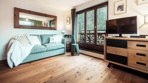 A living room with a sofa, a TV, a wooden cabinet, and a large window with a view of trees. - Vertice - Center Chamonix, Mont-Blanc View (Chamonix-Mont-Blanc)