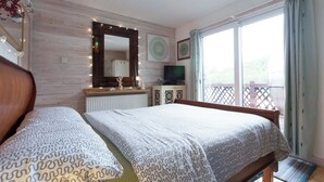 A bedroom with two beds, a large mirror, a television, and a balcony with a view.