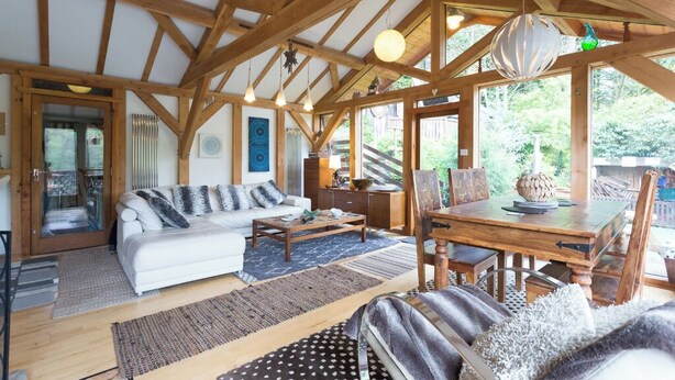 A spacious living area with a wooden ceiling, a sofa, a dining table, and a view of the outdoors.