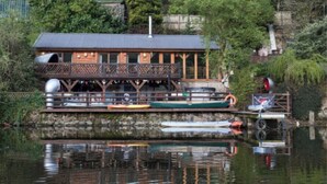 A wooden cabin with a balcony, docked boats, and a stone wall.