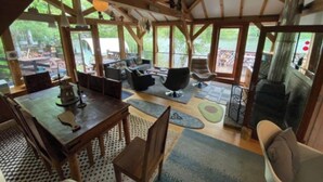 A spacious room with a high ceiling, wooden beams, a dining table with chairs, a sofa, and a fireplace.