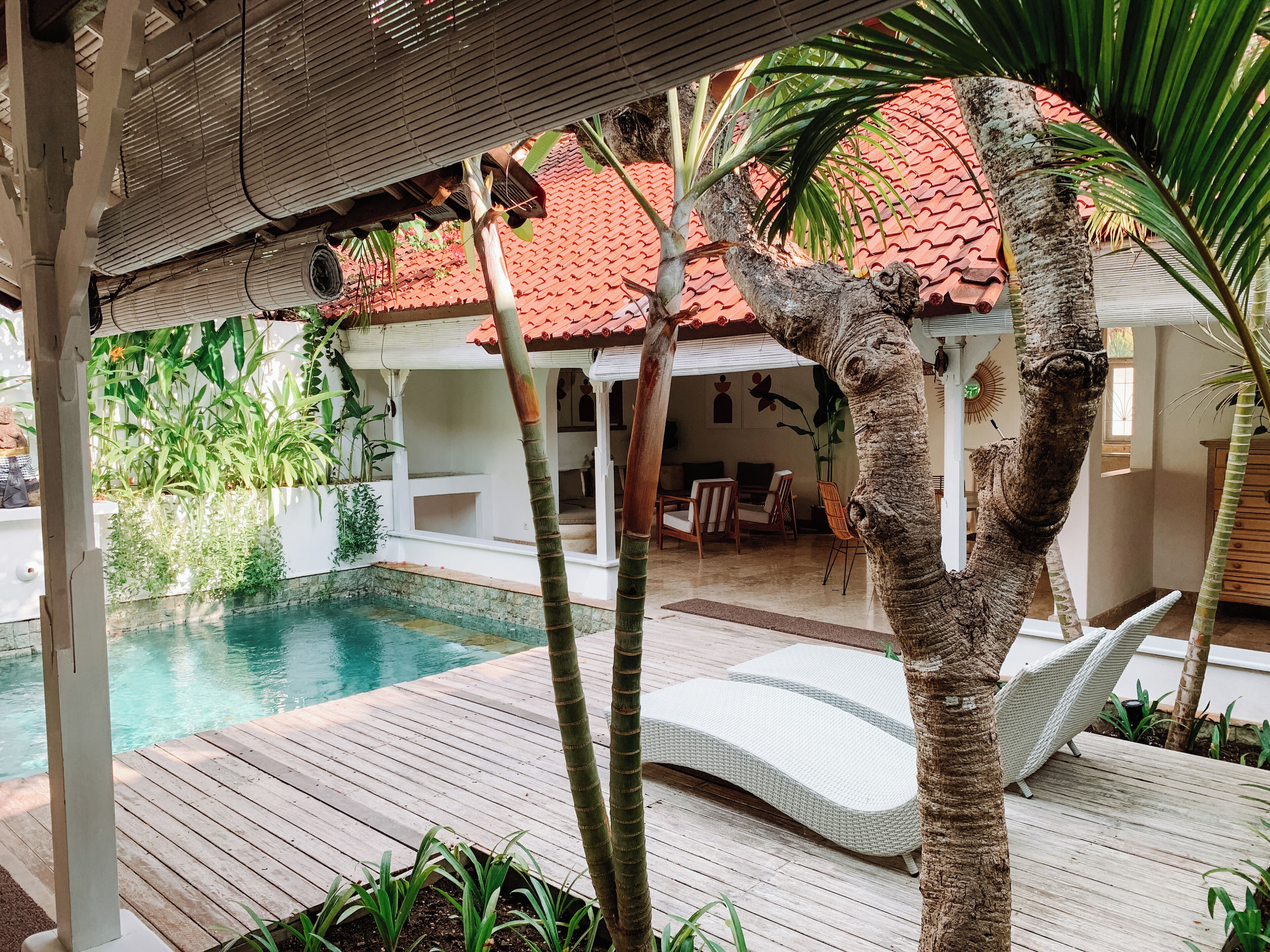 A wooden deck with a pool, lounge chairs, and a covered seating area with a red-tiled roof.