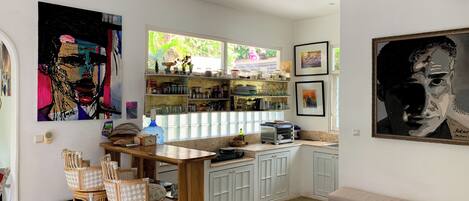 A compact kitchen with a dining area, featuring a large window, a built-in shelf with kitchenware, and a bench.