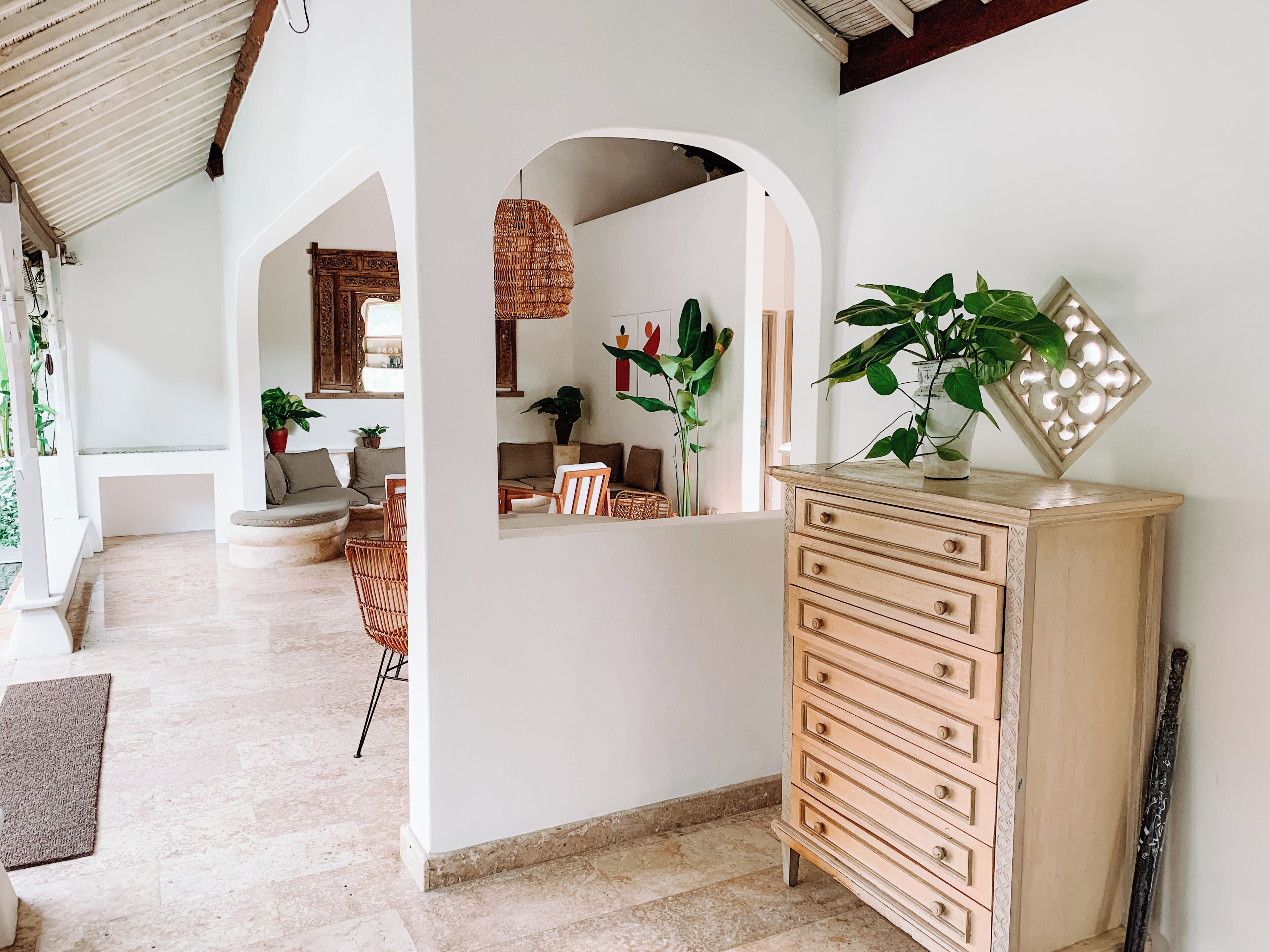 A spacious hallway with a wooden dresser, a woven light fixture, and potted plants.