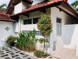 Uma casa com telhado em tijolos, um jardim com plantas e um caminho de cascalho.