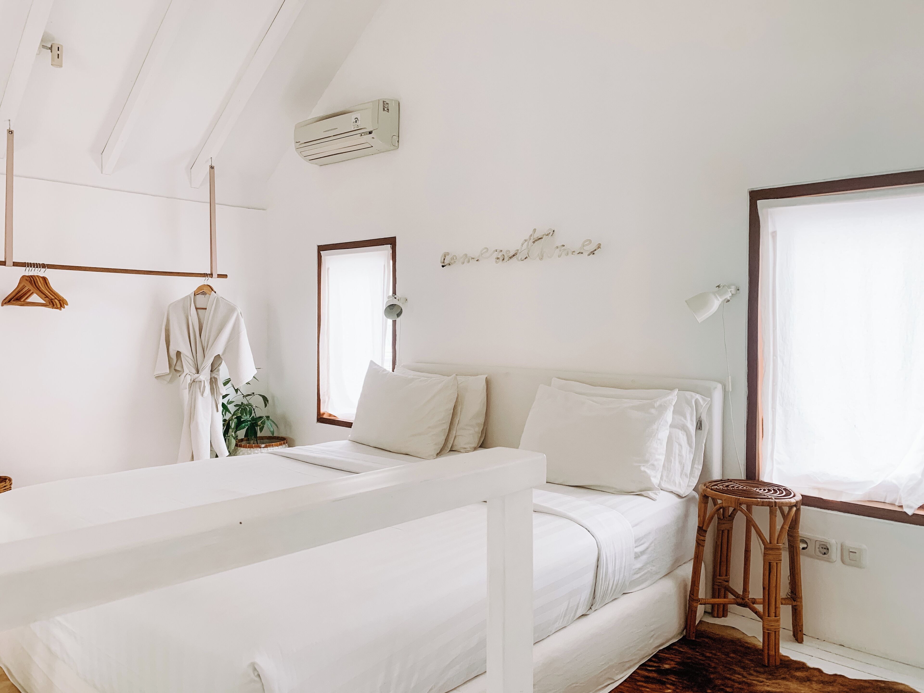 A bedroom with a bunk bed, a bedside table, a mirror, a wall-mounted air conditioner, and a window with curtains.