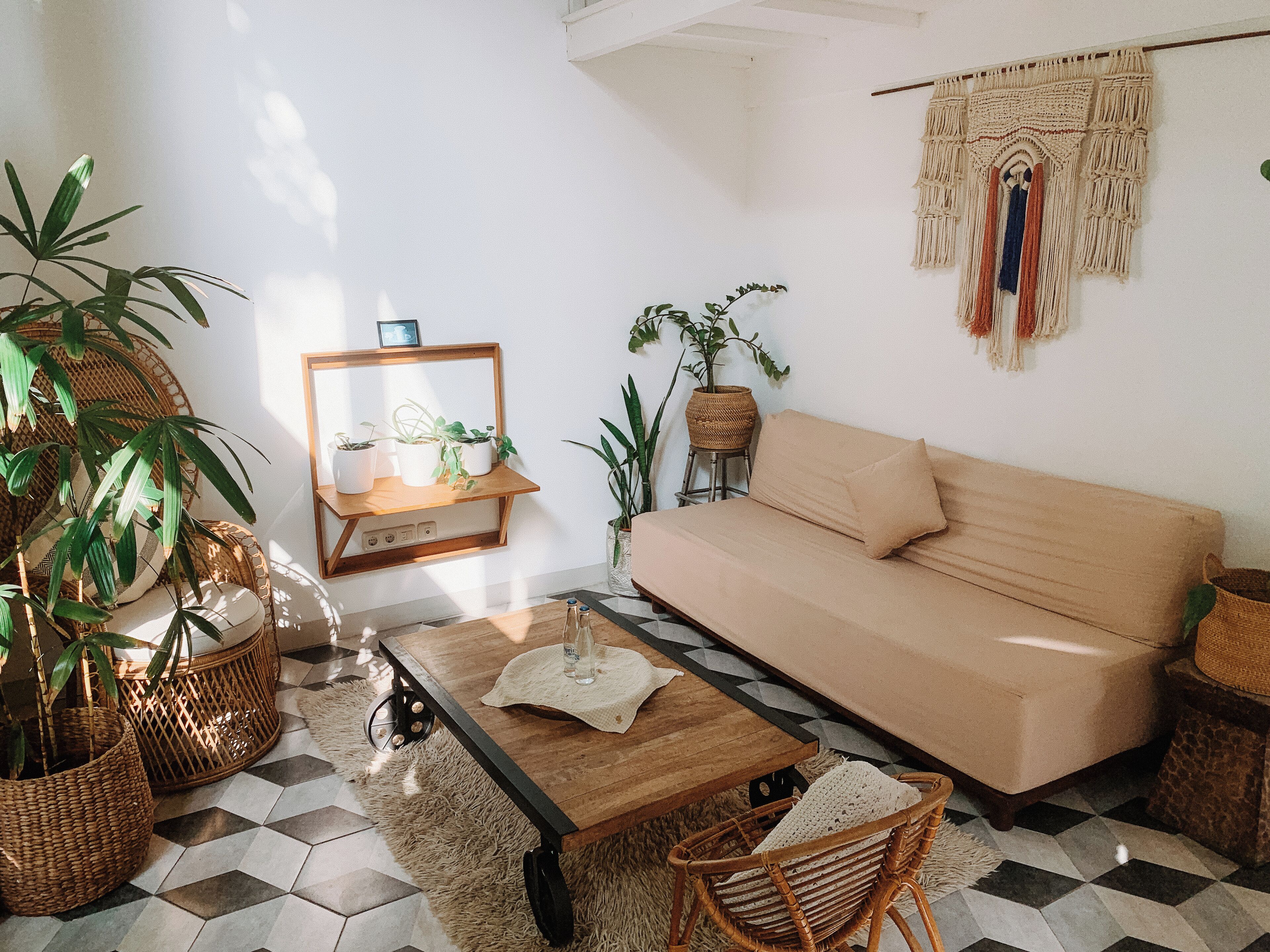 Uma sala de estar com sofá, mesa de centro de madeira, cadeiras de vime e plantas em vasos.