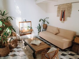 Uma sala de estar com sofá, mesa de centro de madeira, cadeiras de vime e plantas em vasos.