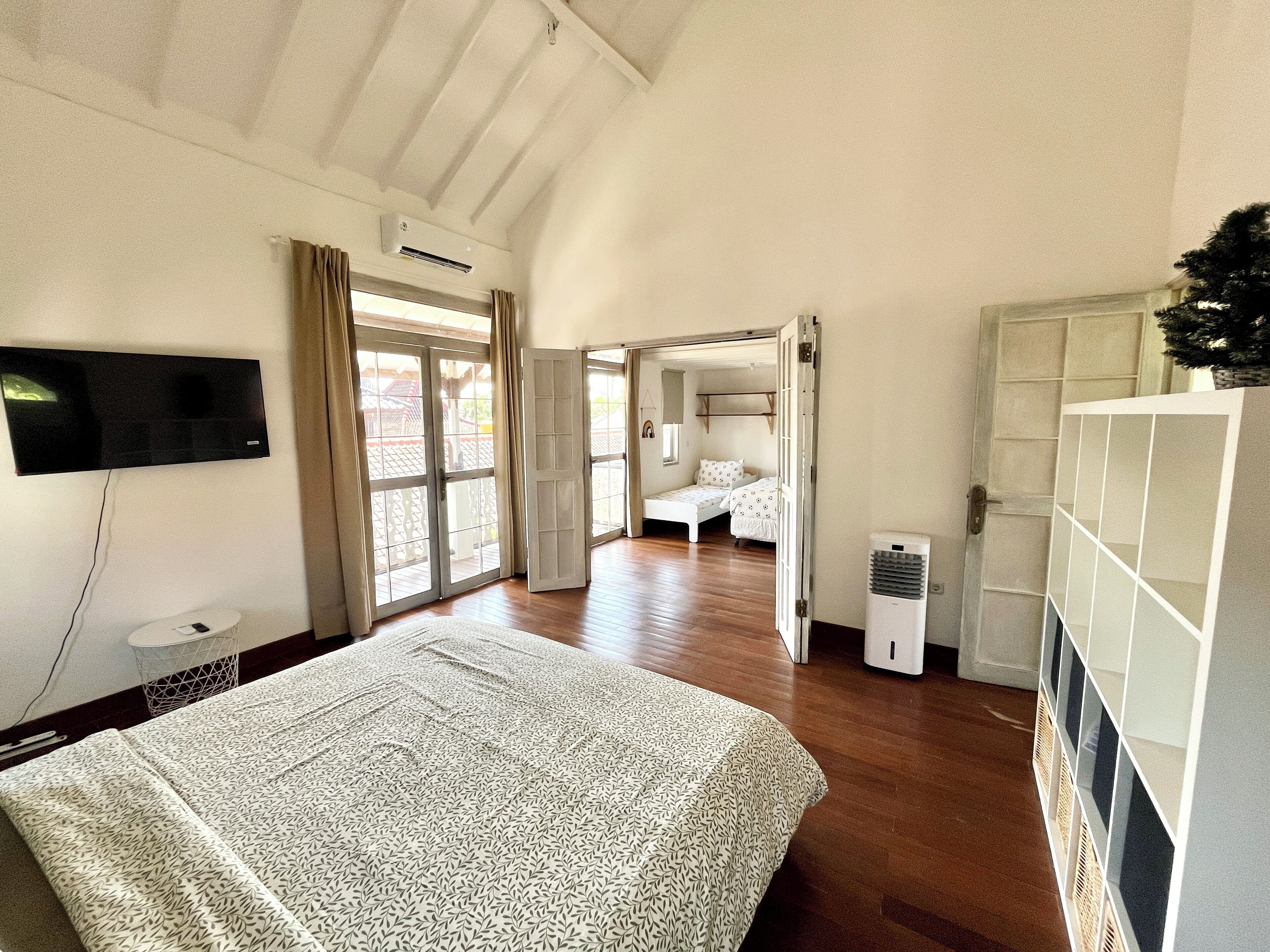 A bedroom with a large bed, a TV mounted on the wall, and a sliding door leading to another room.