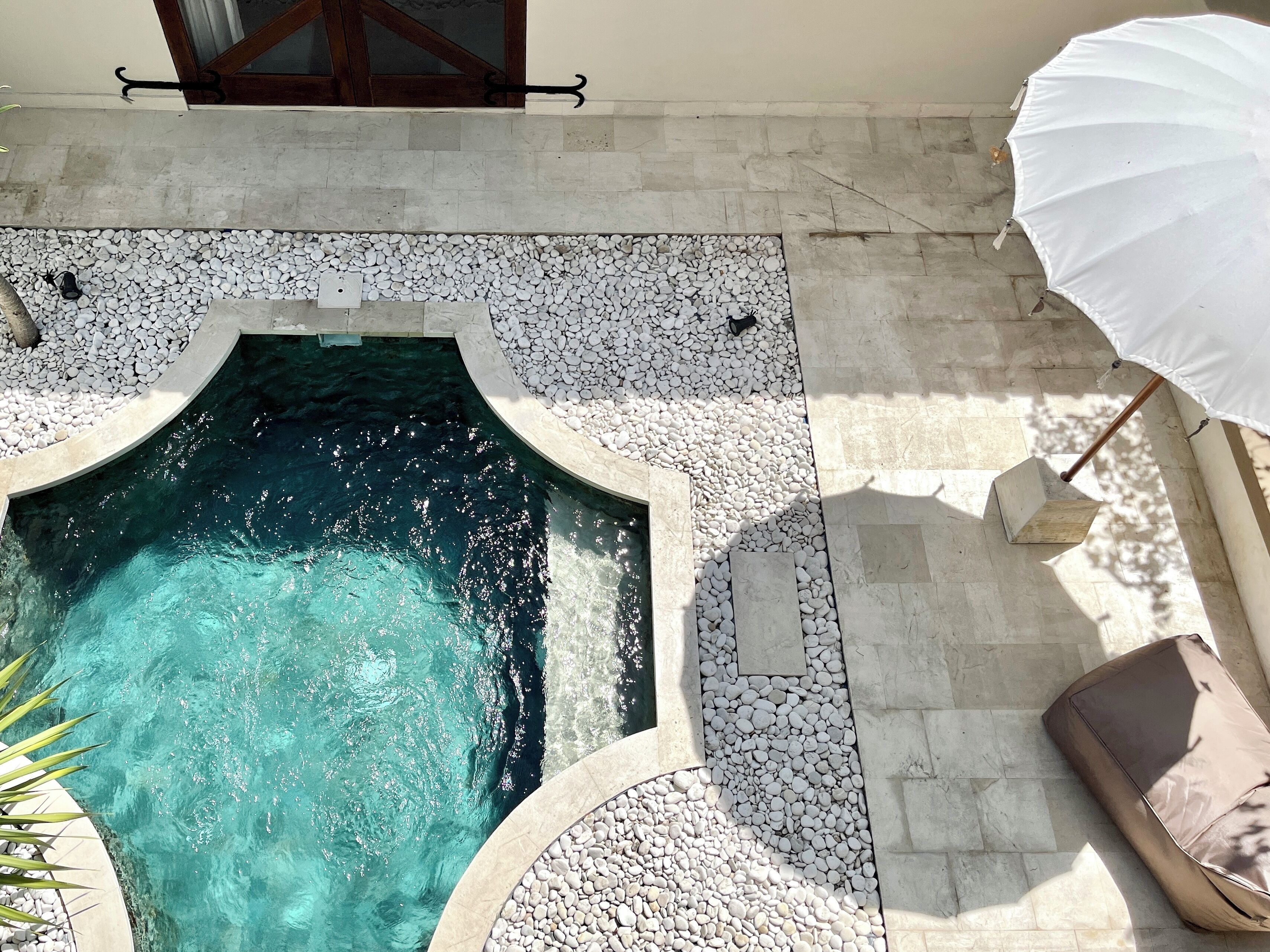 Una piscina con bordo in pietra, un ombrellone bianco e una panchina in pietra.