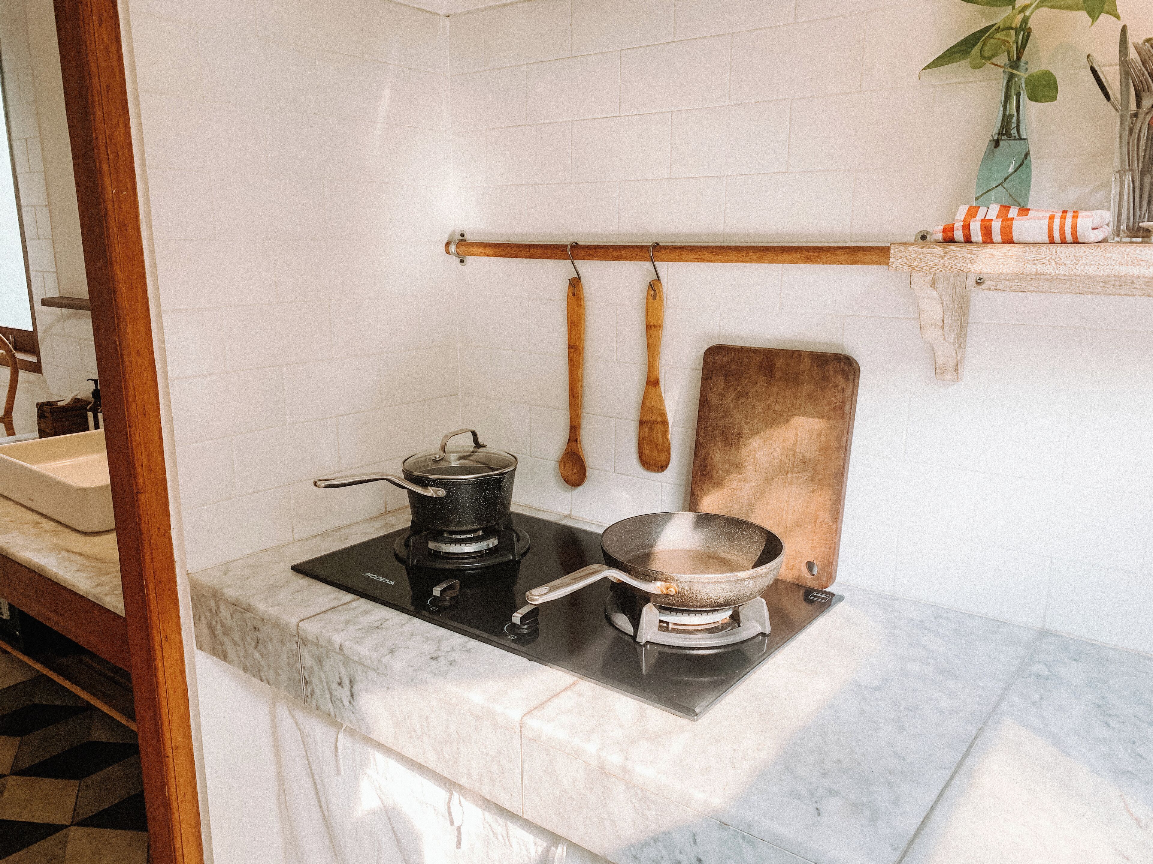 A kitchen with a gas stove, a pot, a pan, wooden utensils, and a cutting board.