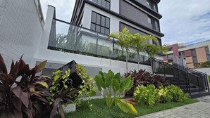 Ein modernes Gebäude mit weißer Fassade, einem Glasbalkon und einem angelegten Garten mit verschiedenen Pflanzen.