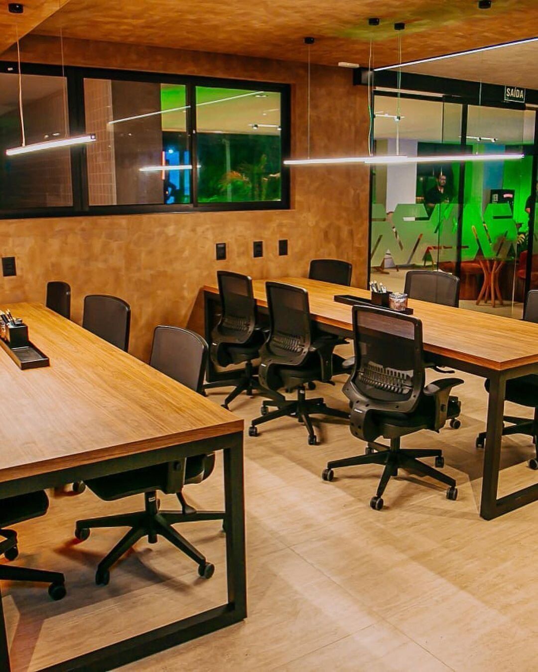 Sala de conferências com uma mesa comprida, cadeiras de escritório pretas e uma parede de vidro com vista para o verde.