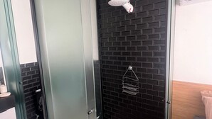 Ein Badezimmer mit schwarzem Fliesenbelag, einer weißen Duschbrause, einem Handtuchhalter und einem Spiegel.