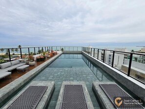 A rooftop infinity pool with a glass edge, surrounded by outdoor seating and a view of the ocean. - Get By Side (João Pessoa)