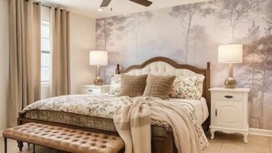 A bedroom with a tufted headboard, a bench at the foot of the bed, two bedside tables with lamps, and a large tree mural on the wall. - The Erin, 1 BR King Duplex by Velvet Ditch Villas (Oxford)