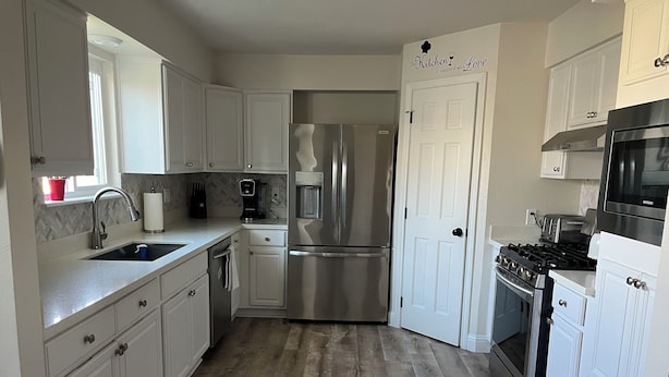 Una cocina moderna con armarios blancos, electrodomésticos de acero inoxidable y un piso de madera con diseño de espiga.