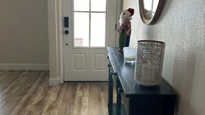 Un pasillo con suelo de madera, una puerta blanca, una consola oscura con un adorno y un espejo en la pared.