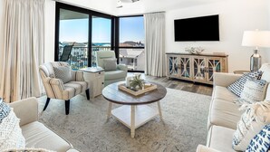 A spacious living room with a large window, a flat-screen TV, a round coffee table, and a sofa.