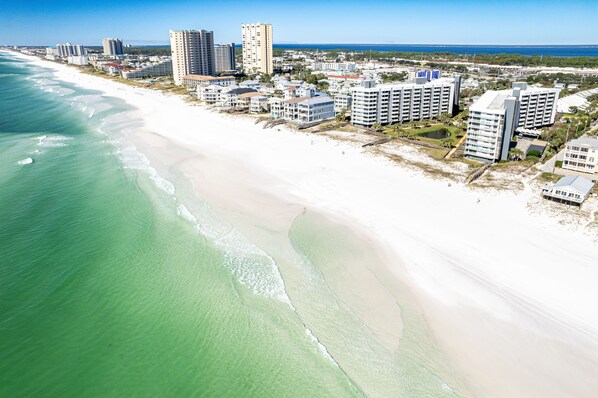 An aerial view of a coastal area with a beachfront hotel complex, including multiple high-rise buildings and a sandy beach.