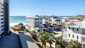 A beachfront residential area with modern buildings, a clear view of the ocean, and a parking lot.