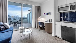 Una habitación de hotel moderna con balcón, kitchenette, sofá y zona de comedor.