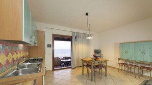 A kitchen with a view to the sea, a dining area with a table and chairs, and a TV. - Villetta Seaside Sardegna (Villaputzu)