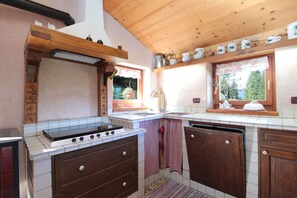 Una cocina con estufa, pileta, gabinetes de madera y ventana con vista a árboles.