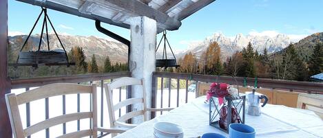 A table set for dining with a mountain view, wooden chairs, and a hanging light fixture.