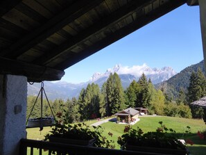 A mountain view from a covered outdoor area with a wooden structure, a small building, and a lawn. - Baita Mountain View Pale San Martino (Fiera Di Primiero)