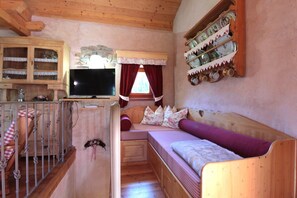 A cozy cabin interior with a wooden staircase, a television, a sofa, and a wall-mounted shelf with decorative items. - Baita Mountain View Pale San Martino (Fiera Di Primiero)