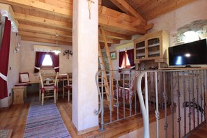 A cozy room with wooden beams, a dining area, a staircase, and a television. - Baita Mountain View Pale San Martino (Fiera Di Primiero)