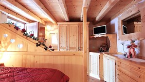 A wooden cabin interior with a bed, cabinets, a TV, and a staircase.