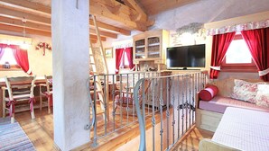 A cozy room with a wooden ceiling, a television, a bed with floral bedding, and a dining area with wooden chairs and a table.