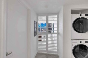 A laundry room with two stacked washing machines, a door with blinds, and a framed picture on the wall. - Icon 2B|2B Fully Remodeled Frontline Bay and Pool (Miami)