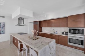 A modern kitchen with a marble island, stainless steel appliances, and wooden cabinets.