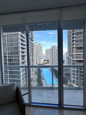 A high-rise apartment with large windows, a view of a swimming pool, and modern buildings in the background.