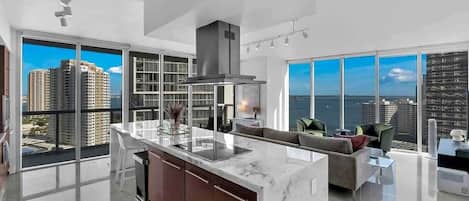 A modern kitchen with a large island, a dining area with a sofa, and large windows offering a city view.