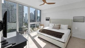 Une chambre moderne avec un grand lit, un ventilateur de plafond, une télévision et une vue sur la ville.