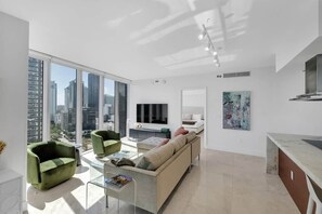 Un salon moderne avec un canapé, des fauteuils, une table basse, un téléviseur et des œuvres d’art accrochées aux murs.