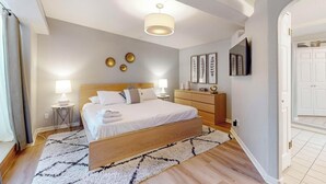 A modern bedroom with a wooden bed, bedside lamps, a dresser, and a flat-screen TV on the wall. - Bright 3bd/2.5b Home w/Garage, Dog, Firepit (Albuquerque)