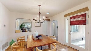 A dining area with a wooden table, six chairs, a chandelier, and a red window blind. - Bright 3bd/2.5b Home w/Garage, Dog, Firepit (Albuquerque)